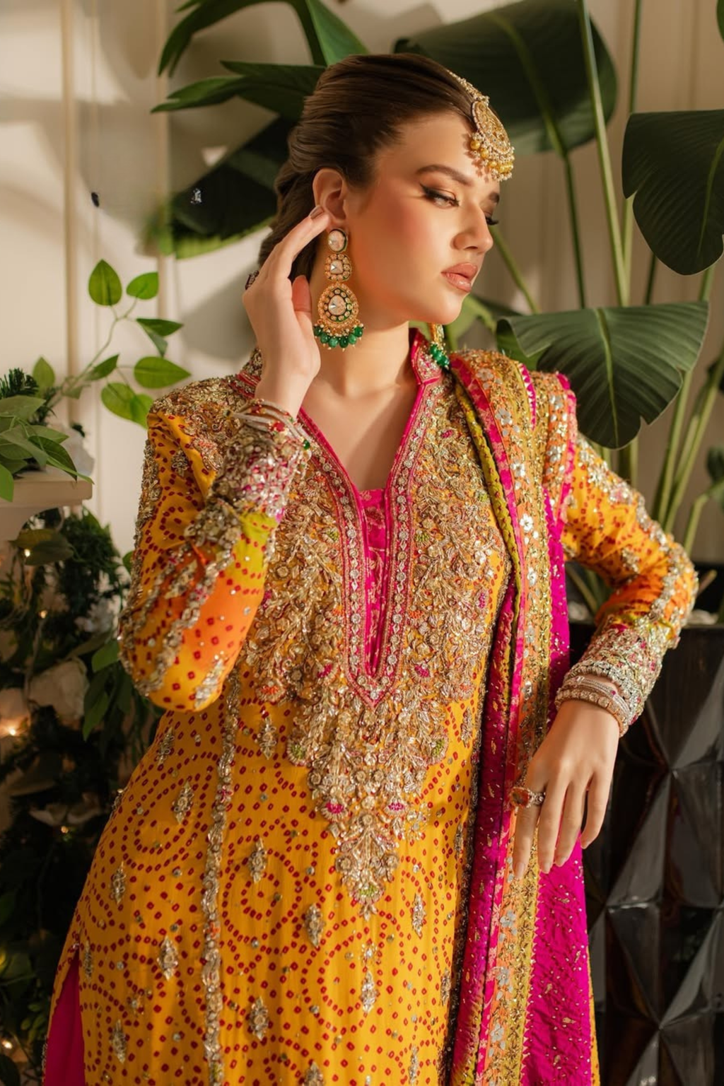 Woman in a traditional embroidered outfit with vibrant colors against a plant-filled background
