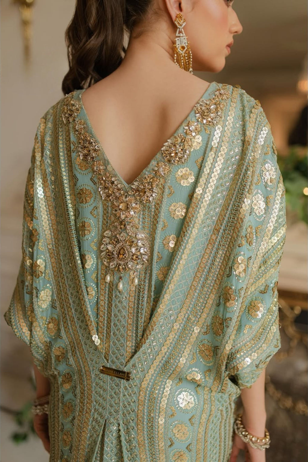 Woman wearing a light blue embroidered dress with gold details.