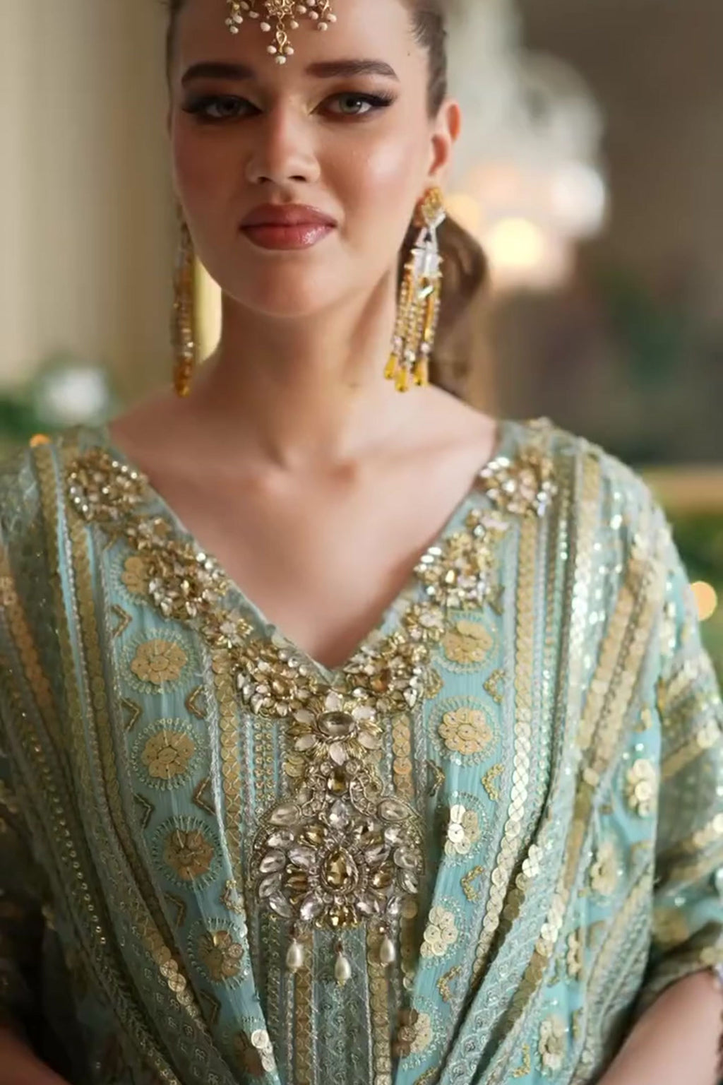 Woman wearing an ornate, light green dress with gold embroidery and jewelry.