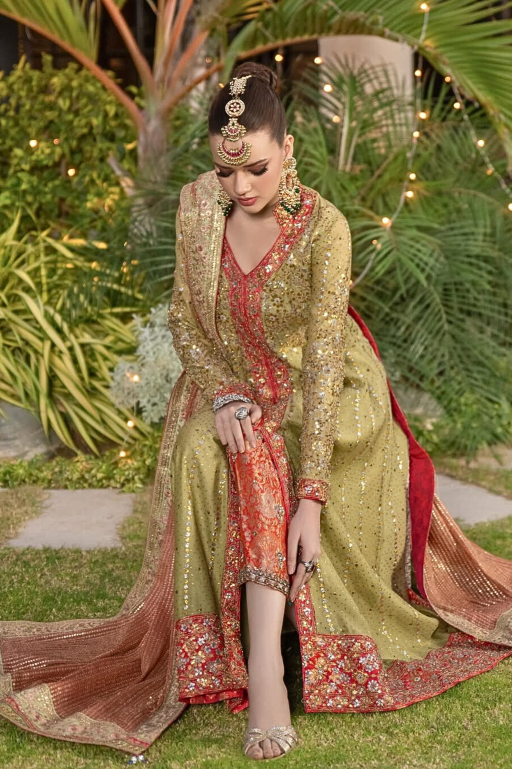 Woman in traditional embroidered outfit with jewelry, sitting outdoors.