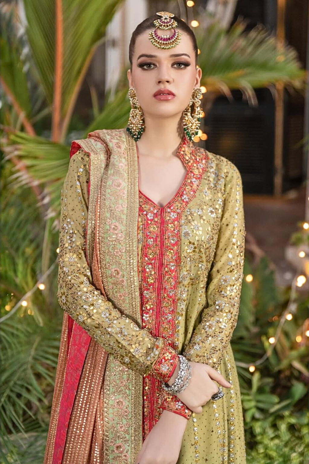 Woman in traditional embroidered outfit with jewelry against a green foliage background