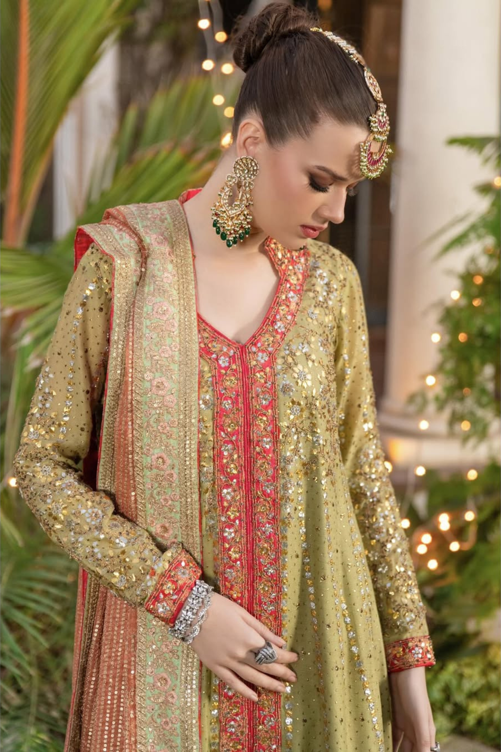 Woman in traditional embroidered outfit with jewelry, surrounded by plants and lights