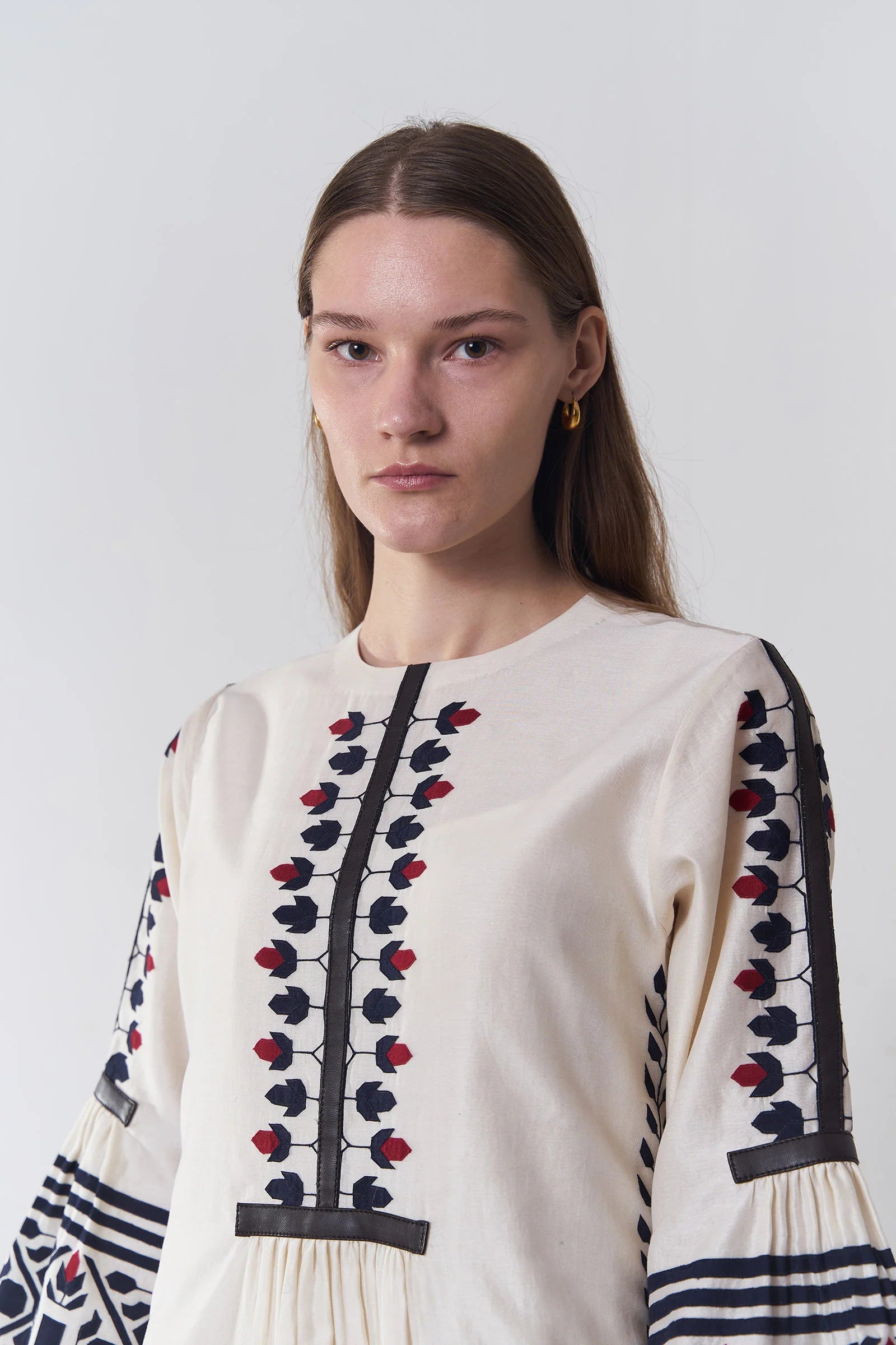 an russian model wearing An ivory floor-length Chanderi dress featuring dramatic bell sleeves and vertical panels of tonal geometric hand-cut appliqué.