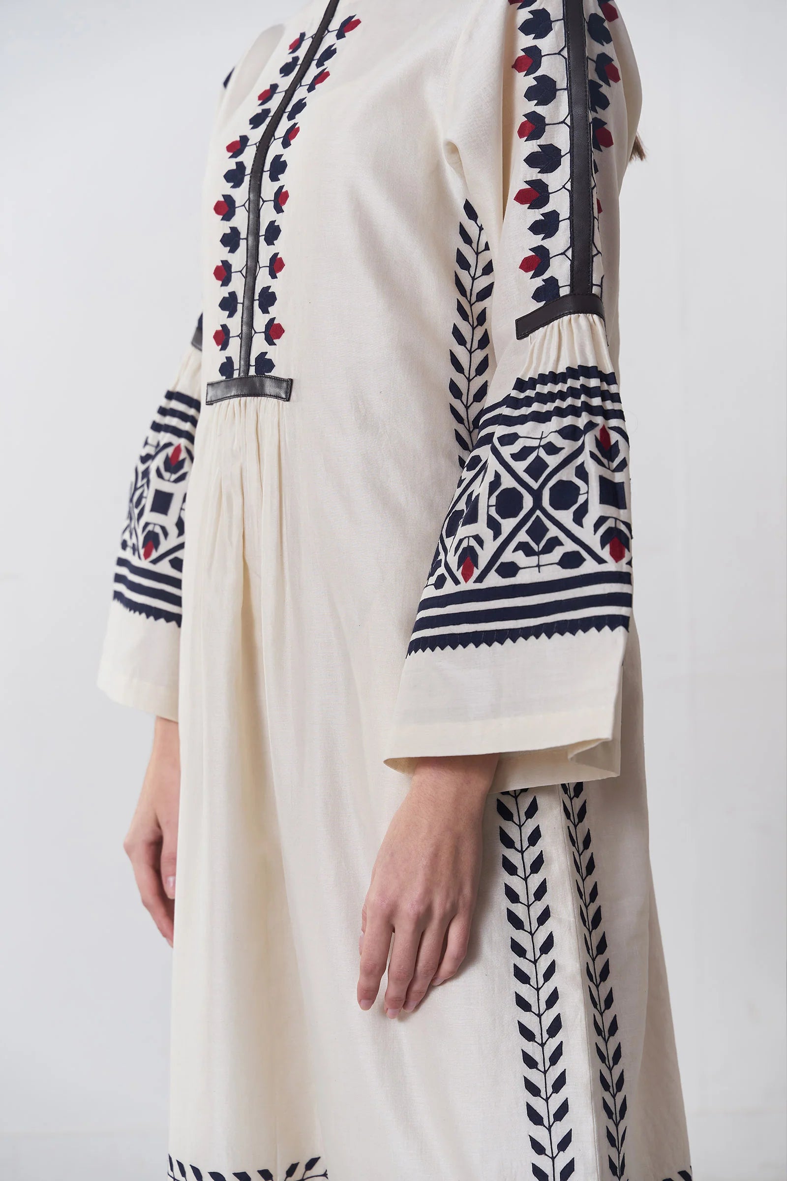 an russian model wearing An ivory floor-length Chanderi dress featuring dramatic bell sleeves and vertical panels of tonal geometric hand-cut appliqué.