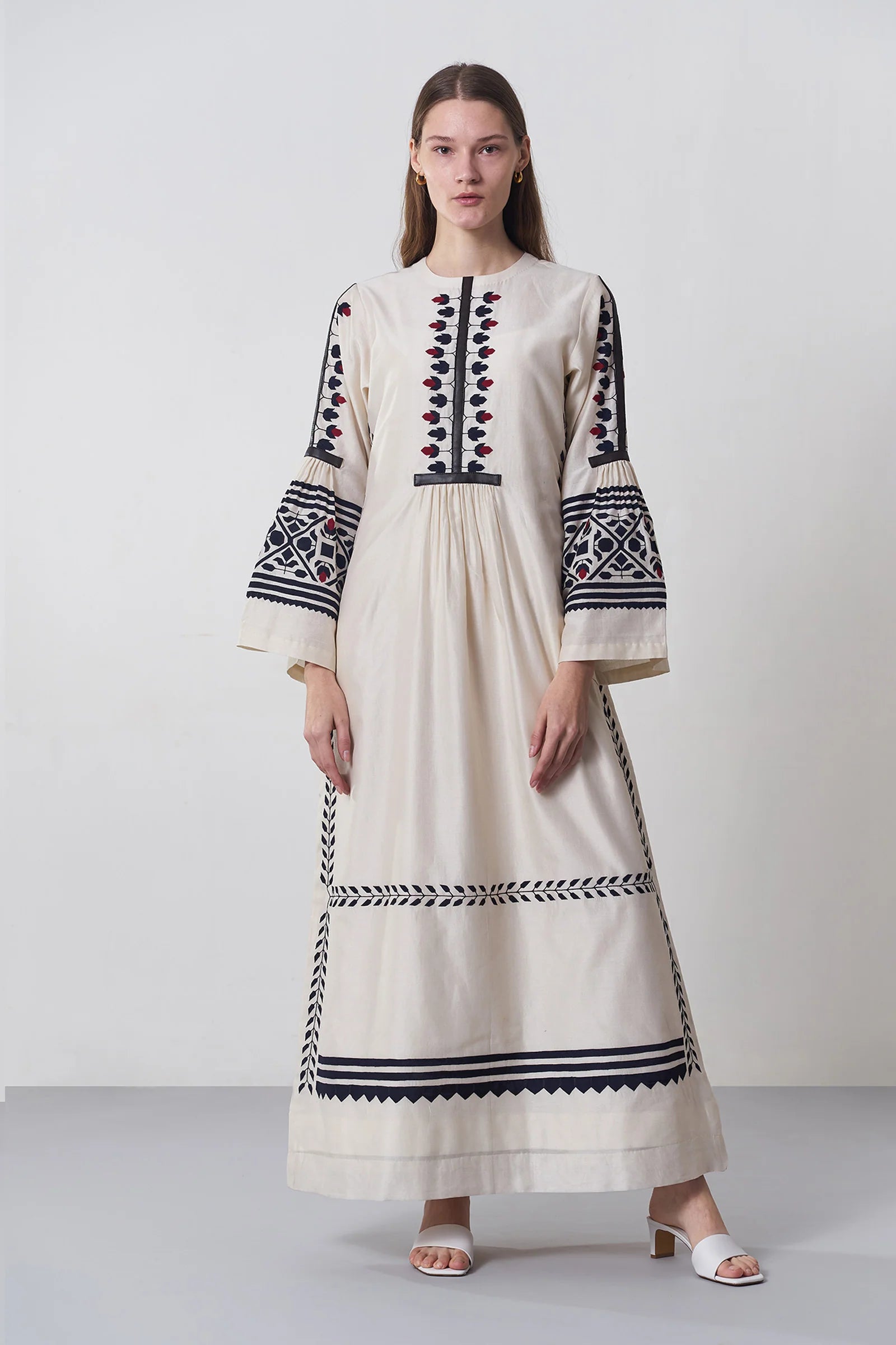 an russian model wearing An ivory floor-length Chanderi dress featuring dramatic bell sleeves and vertical panels of tonal geometric hand-cut appliqué.
