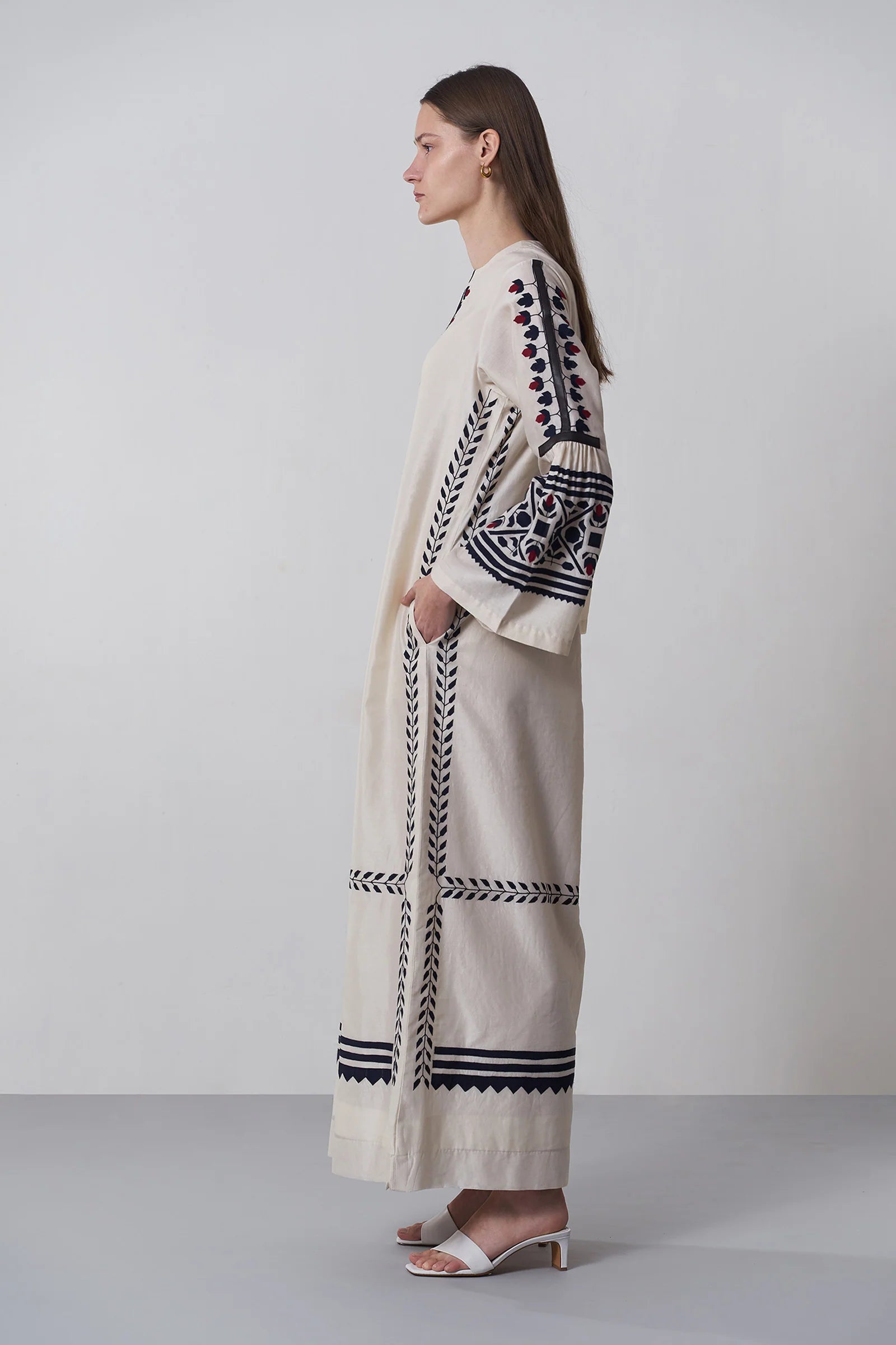 an russian model wearing An ivory floor-length Chanderi dress featuring dramatic bell sleeves and vertical panels of tonal geometric hand-cut appliqué.