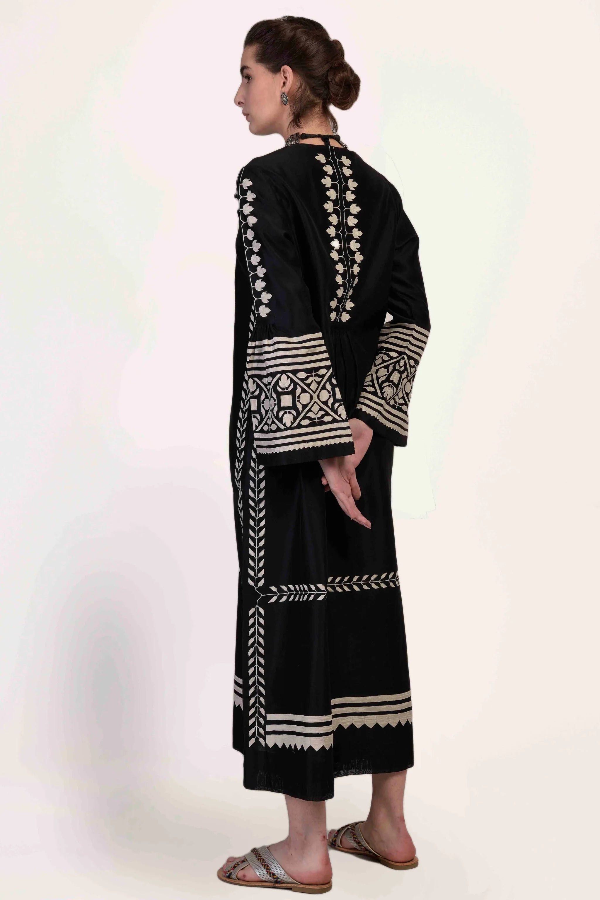 A floor-length black Chanderi dress featuring dramatic bell sleeves and vertical panels of ivory geometric hand-cut appliqué along the bodice and sleeves.