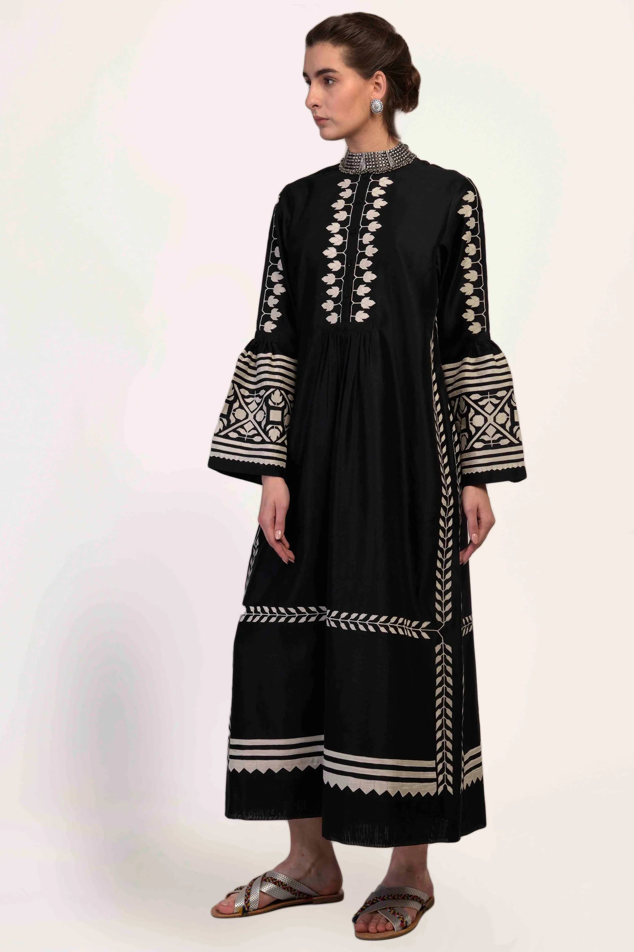 A floor-length black Chanderi dress featuring dramatic bell sleeves and vertical panels of ivory geometric hand-cut appliqué along the bodice and sleeves.