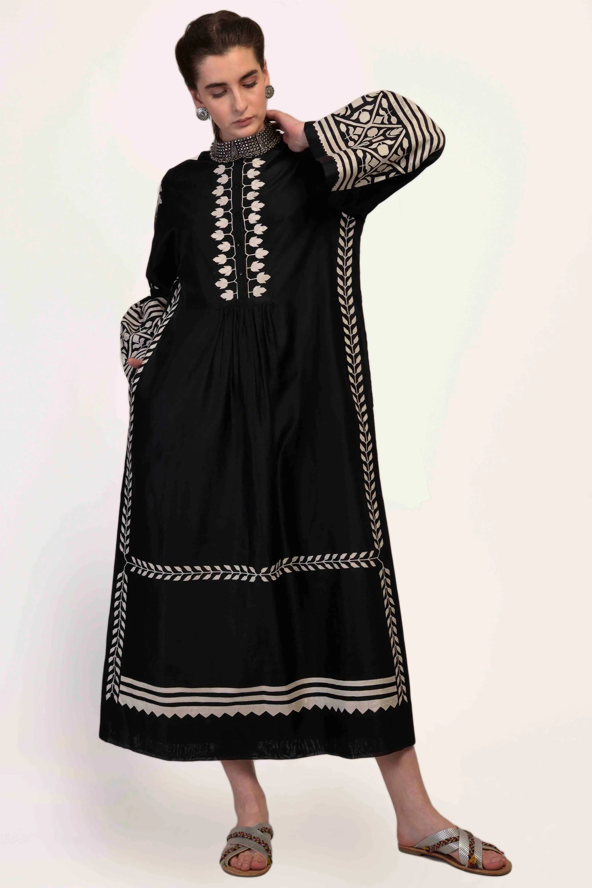 A floor-length black Chanderi dress featuring dramatic bell sleeves and vertical panels of ivory geometric hand-cut appliqué along the bodice and sleeves.