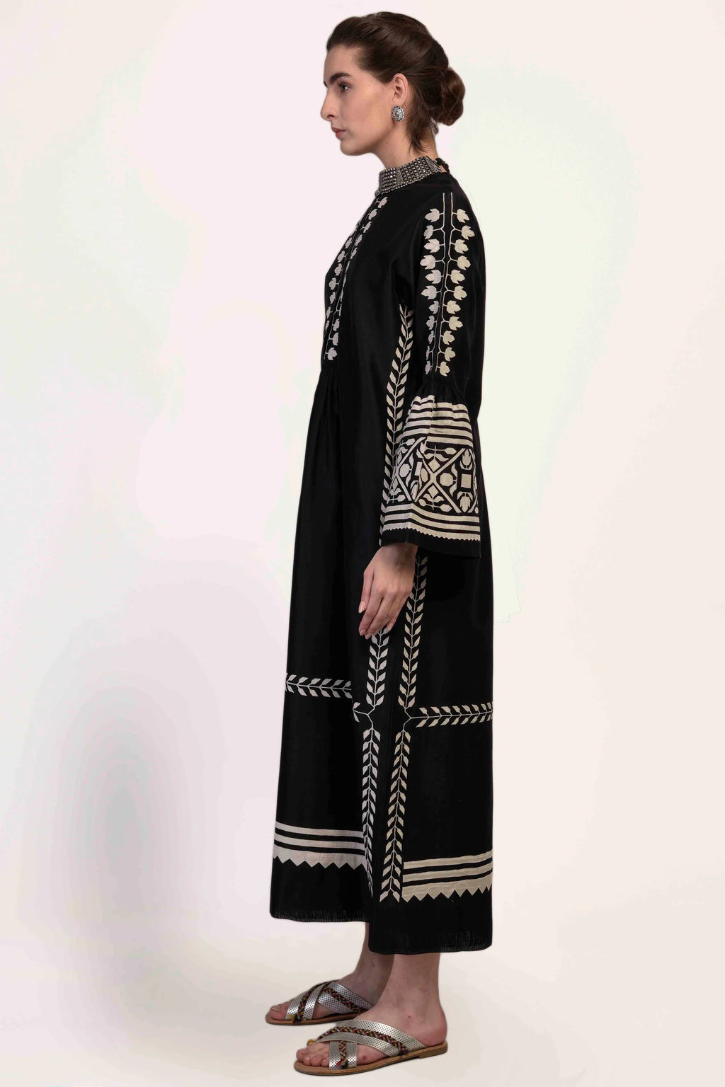 A floor-length black Chanderi dress featuring dramatic bell sleeves and vertical panels of ivory geometric hand-cut appliqué along the bodice and sleeves.