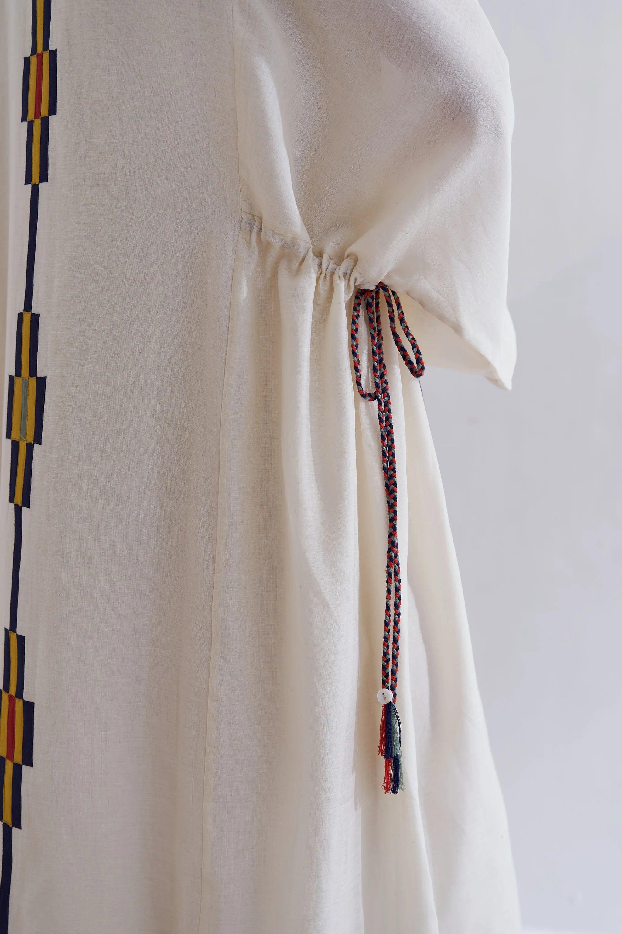 A model in a cream Cotton Silk Chanderi kaftan dress with vertical green stripes and a complex geometric multi-colored appliqué panel on the front and back.
