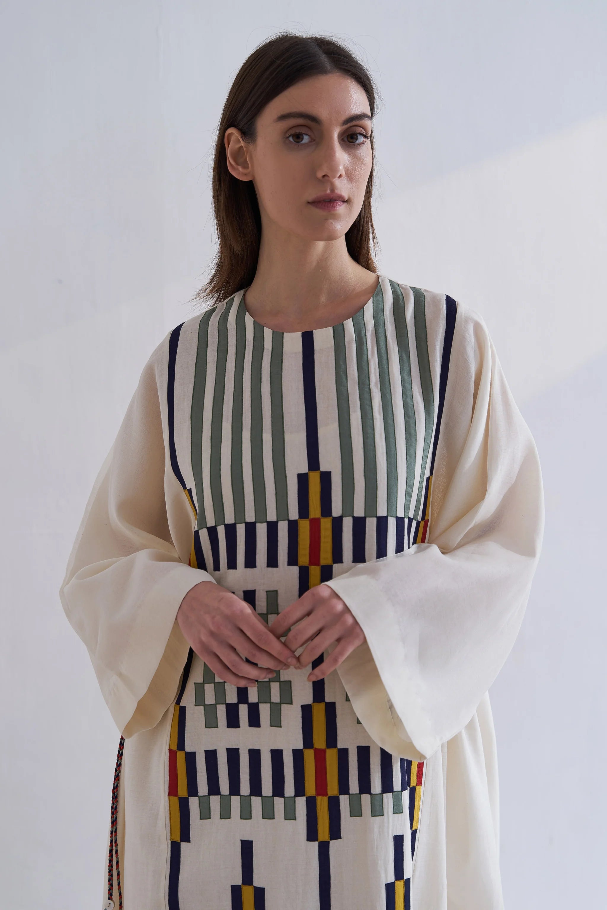 A model in a cream Cotton Silk Chanderi kaftan dress with vertical green stripes and a complex geometric multi-colored appliqué panel on the front and back.