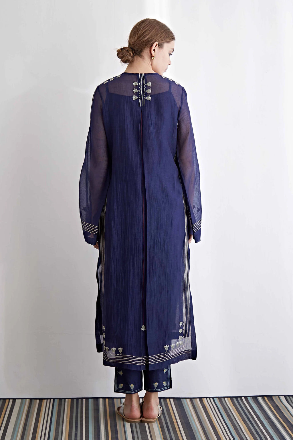 Woman wearing a long dark blue embroidered dress with a plain white background
