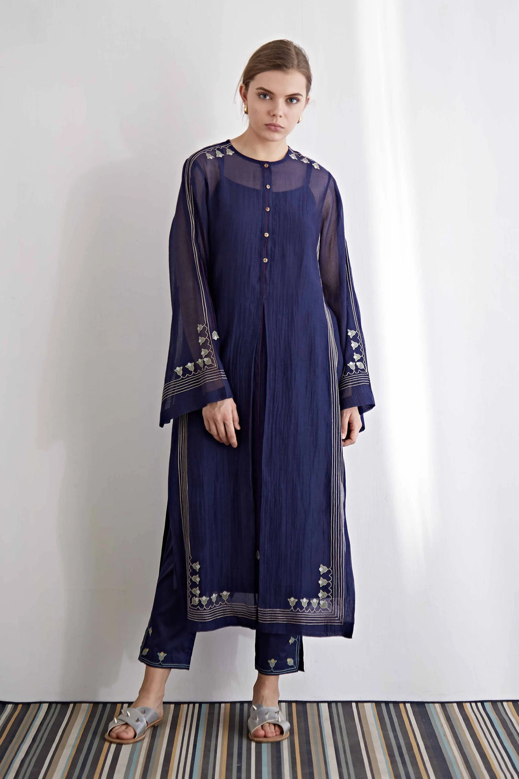 A model in a navy blue long kameez with center pleat detailing and white floral hand-cut appliqué along the hem and sleeves.
