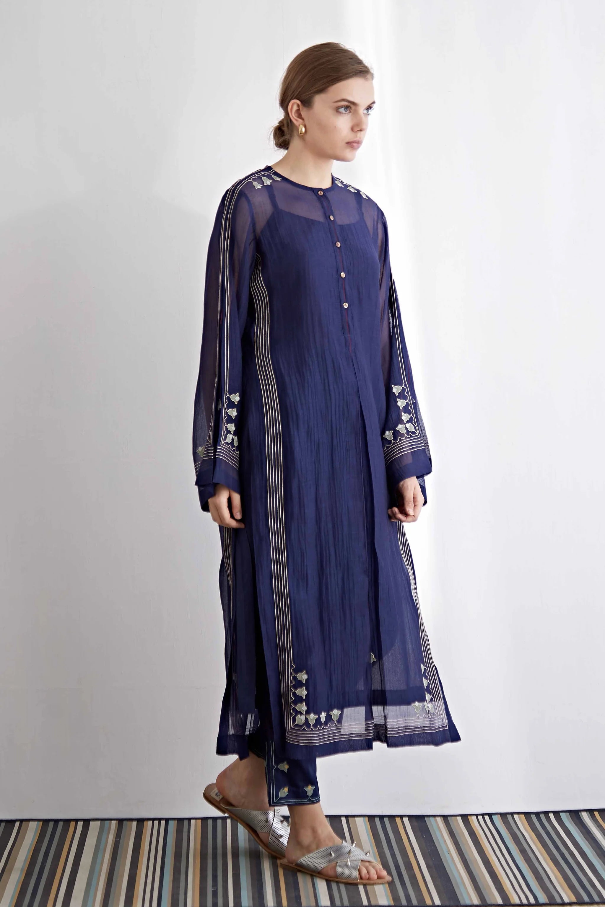 A model in a navy blue long kameez with center pleat detailing and white floral hand-cut appliqué along the hem and sleeves.