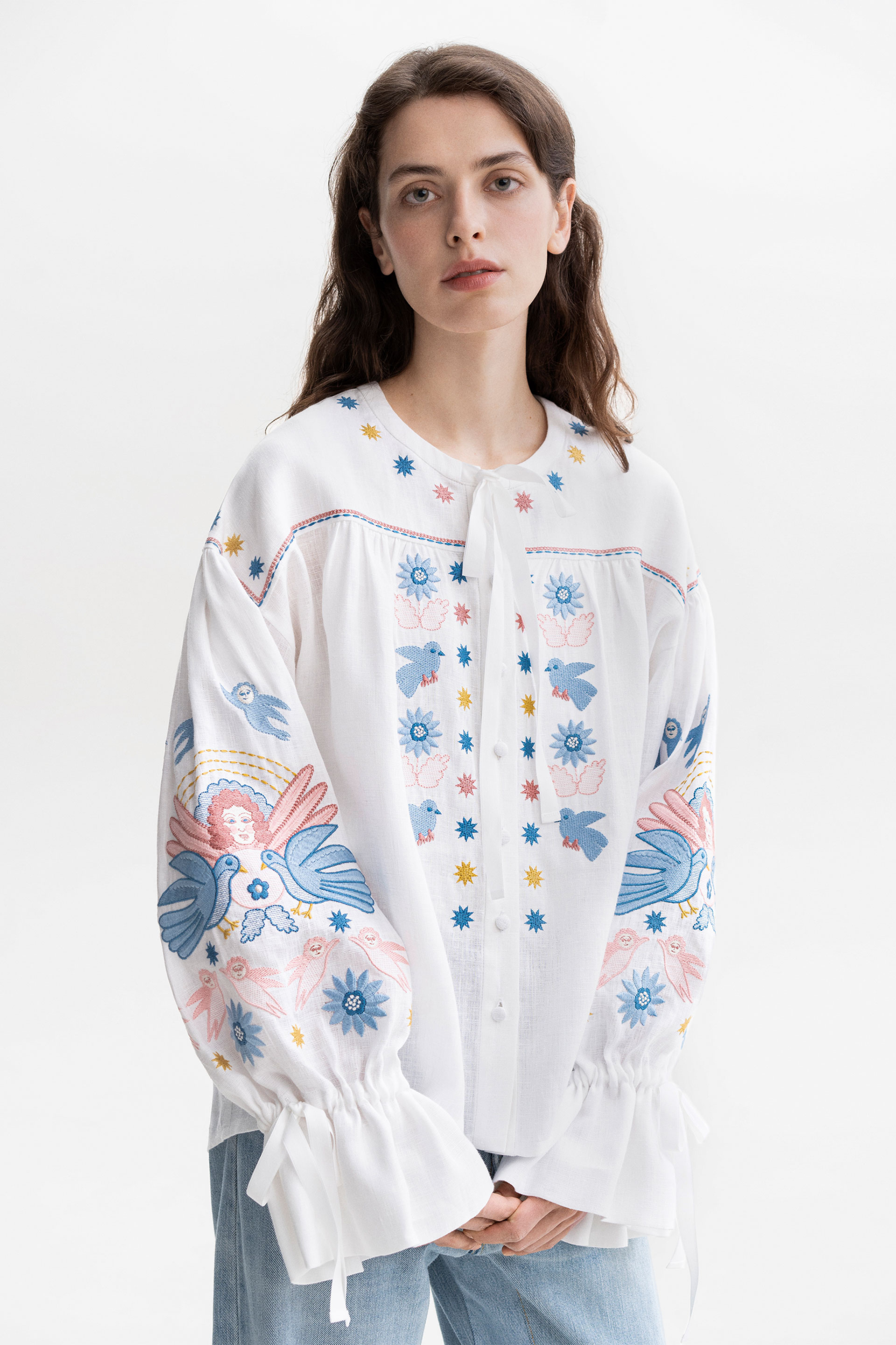 Woman wearing a white floral embroidered blouse with floral patterns on a white background