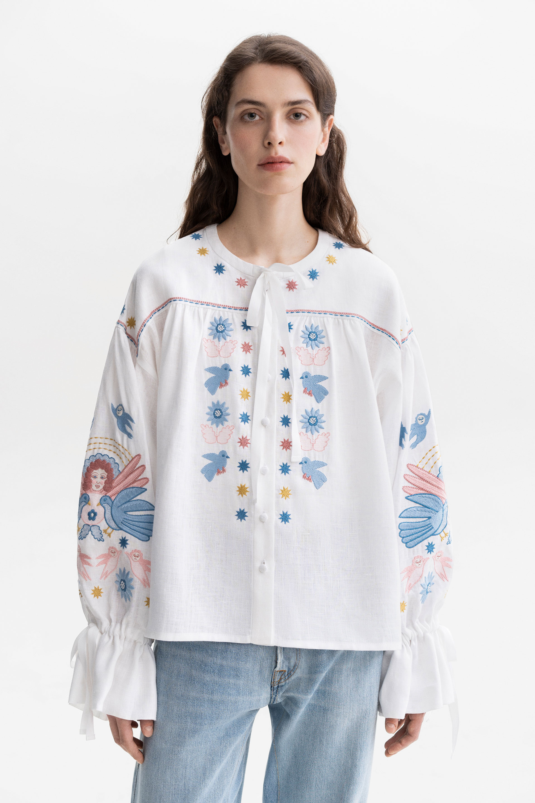 Woman wearing a white embroidered blouse with floral patterns on a white background