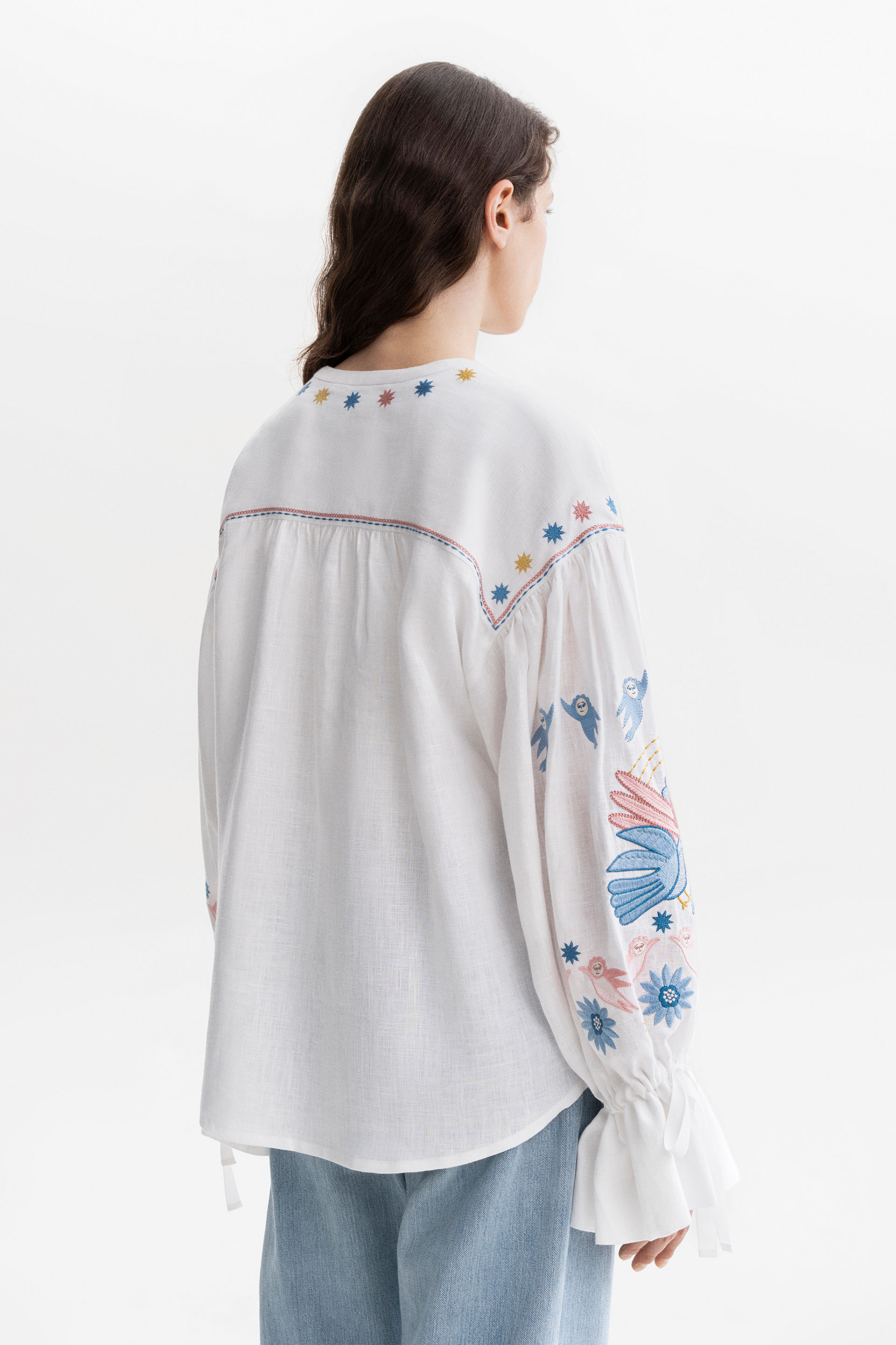 Woman wearing a white embroidered blouse with floral patterns on a white background
