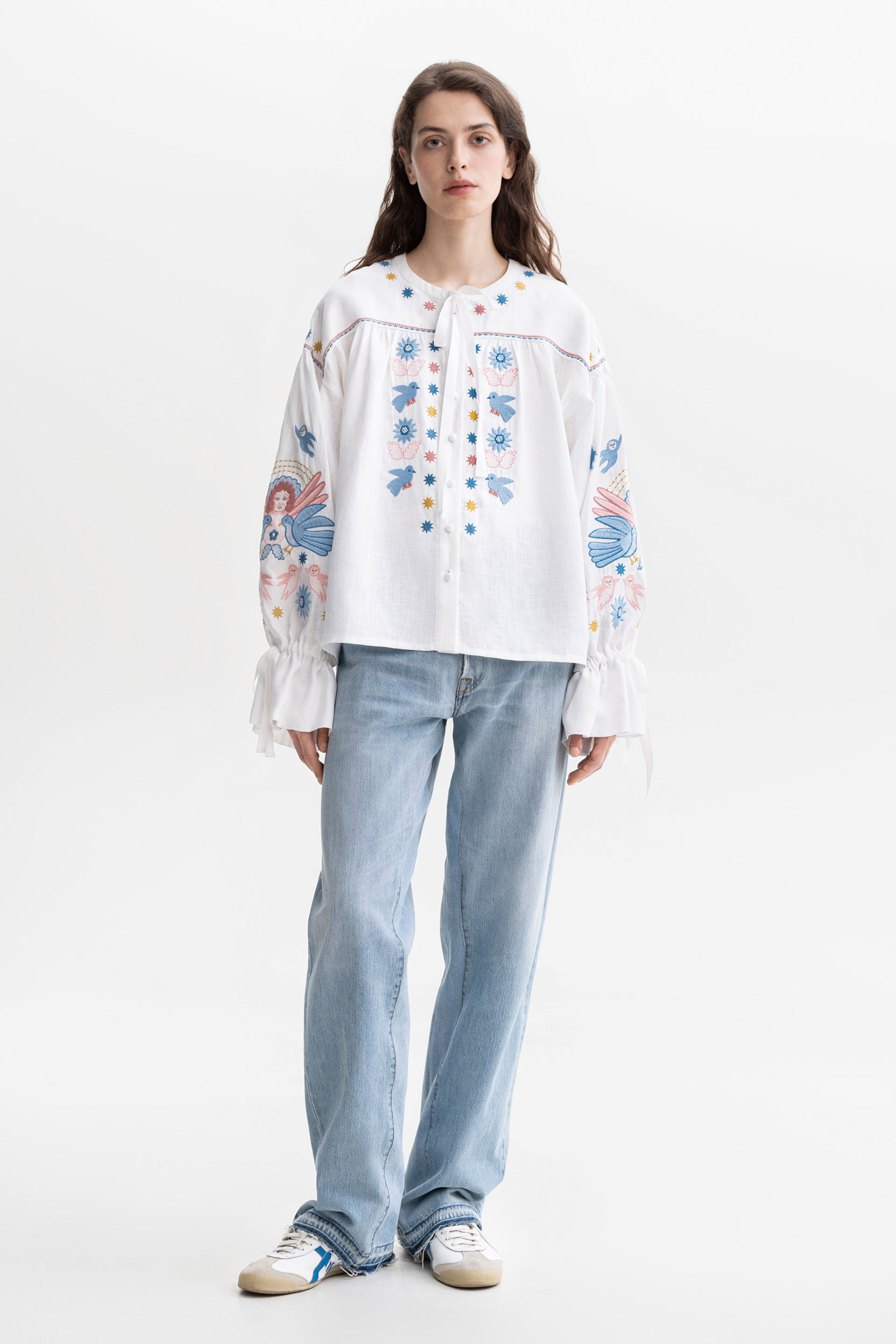 Woman wearing a white embroidered blouse with floral patterns on a white background