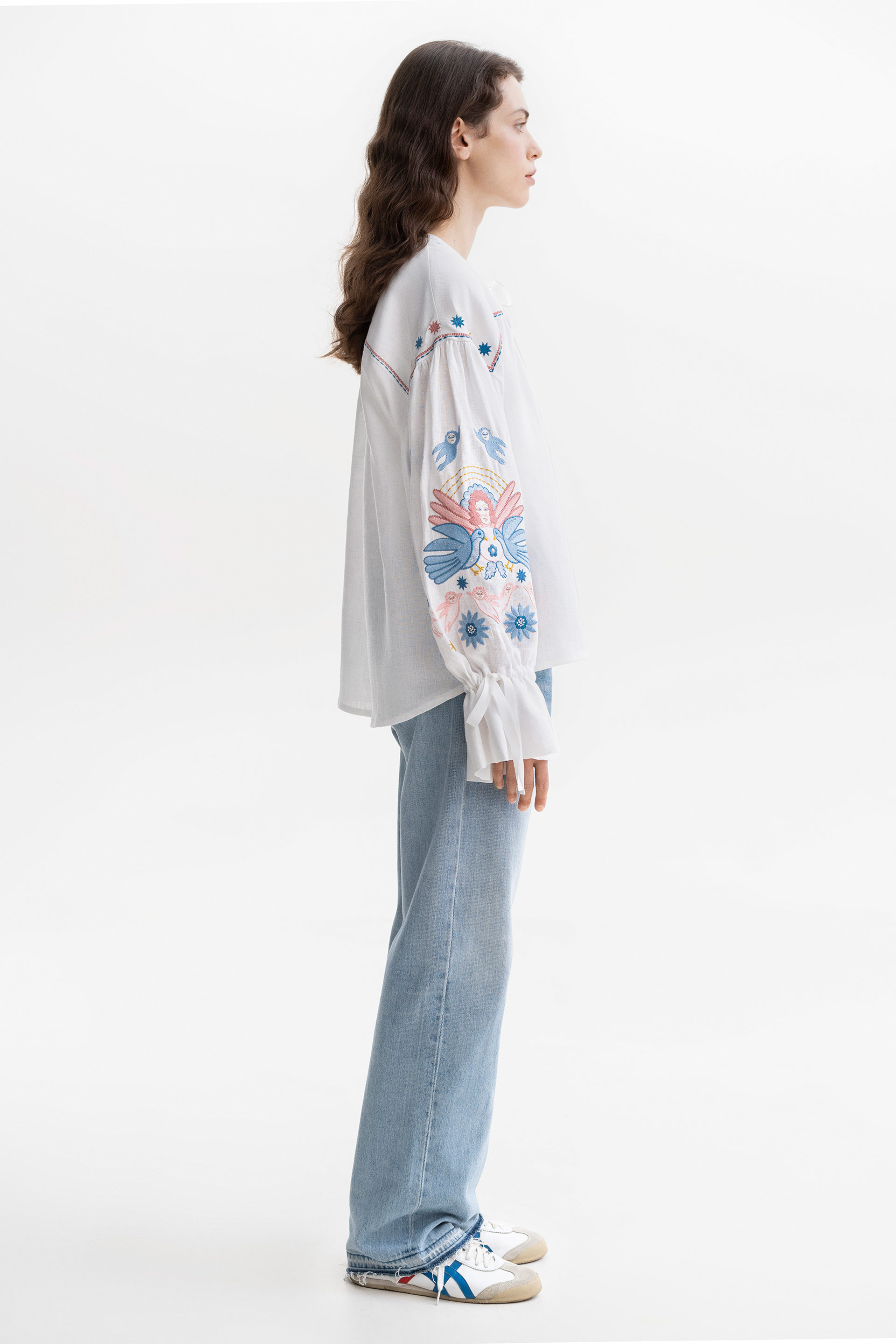 Woman wearing a white embroidered blouse with floral patterns on a white background