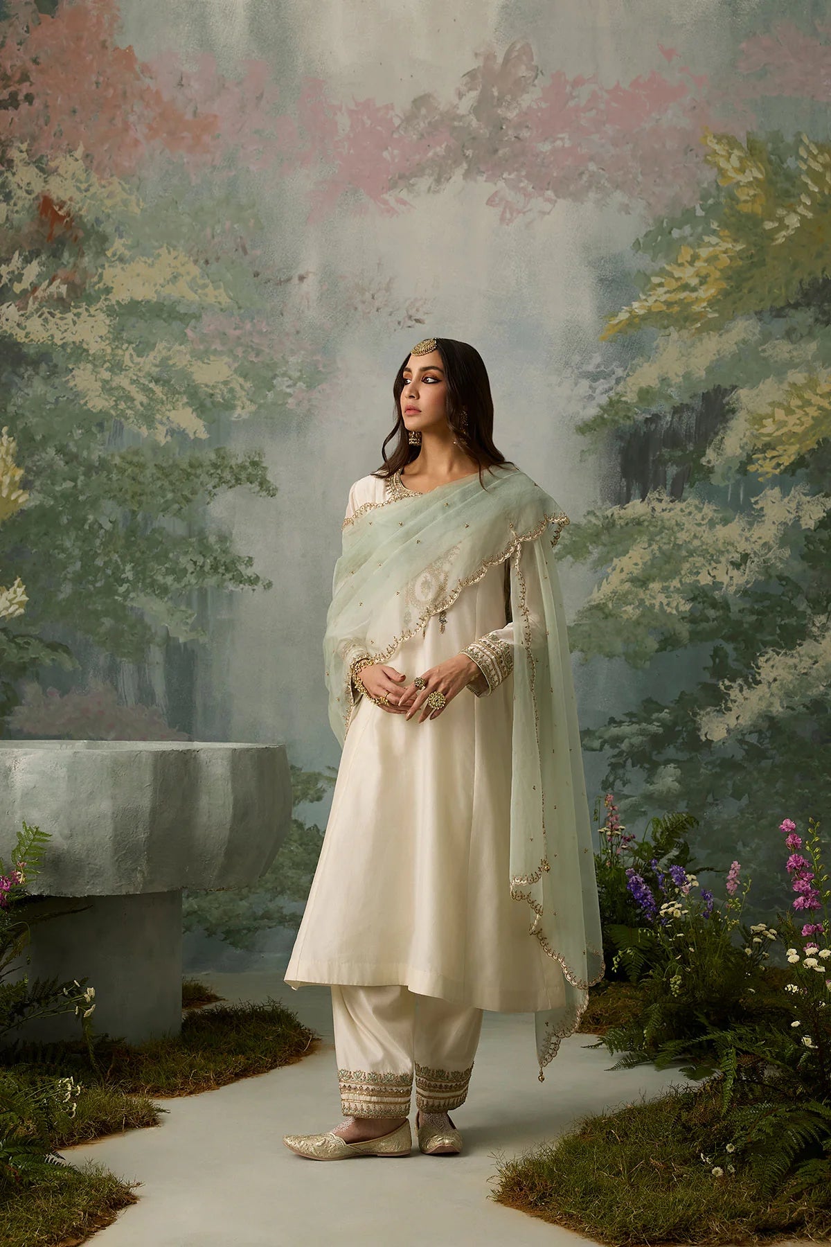 Woman in a traditional outfit standing in a garden with a painted wall in the background
