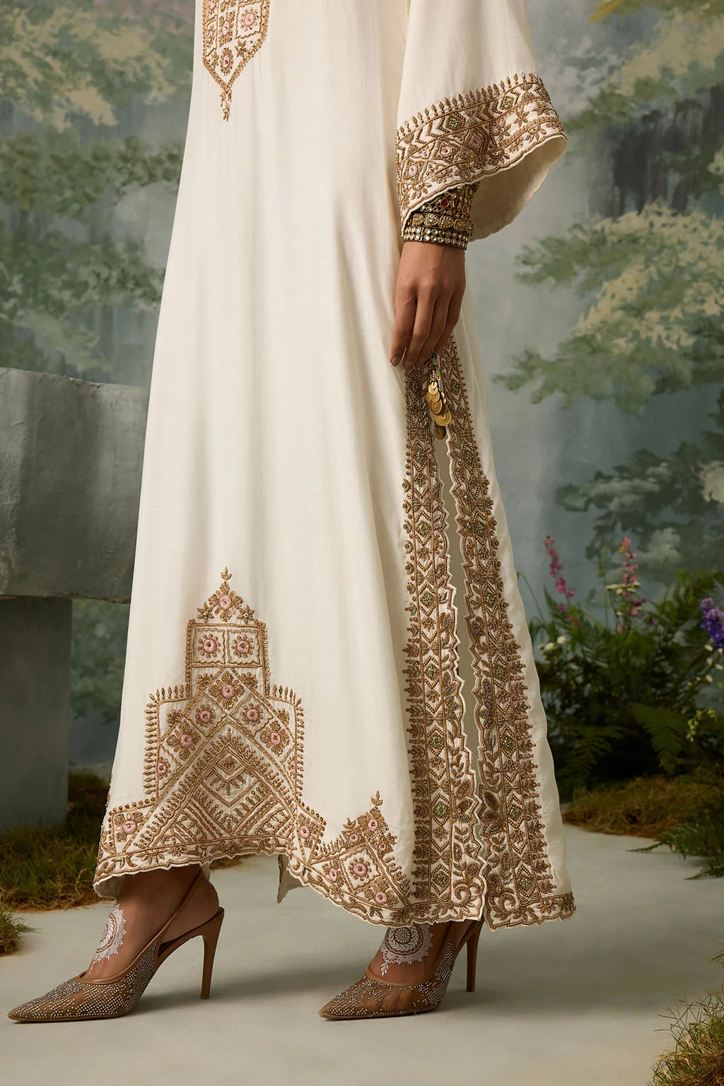 White dress with intricate brown embroidery worn by a person, set against a natural background.