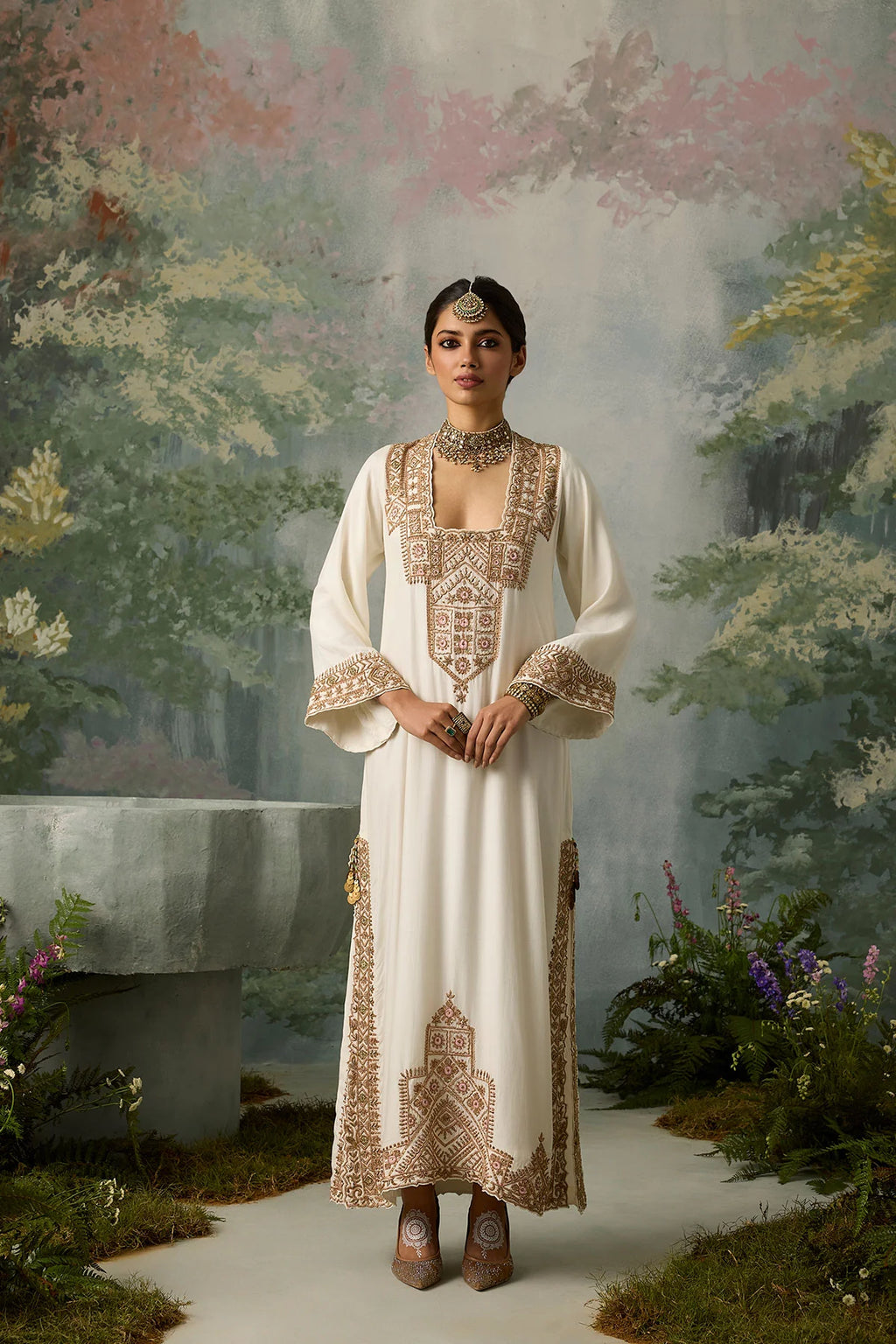 Woman in an embroidered dress standing in a garden with a painted landscape background