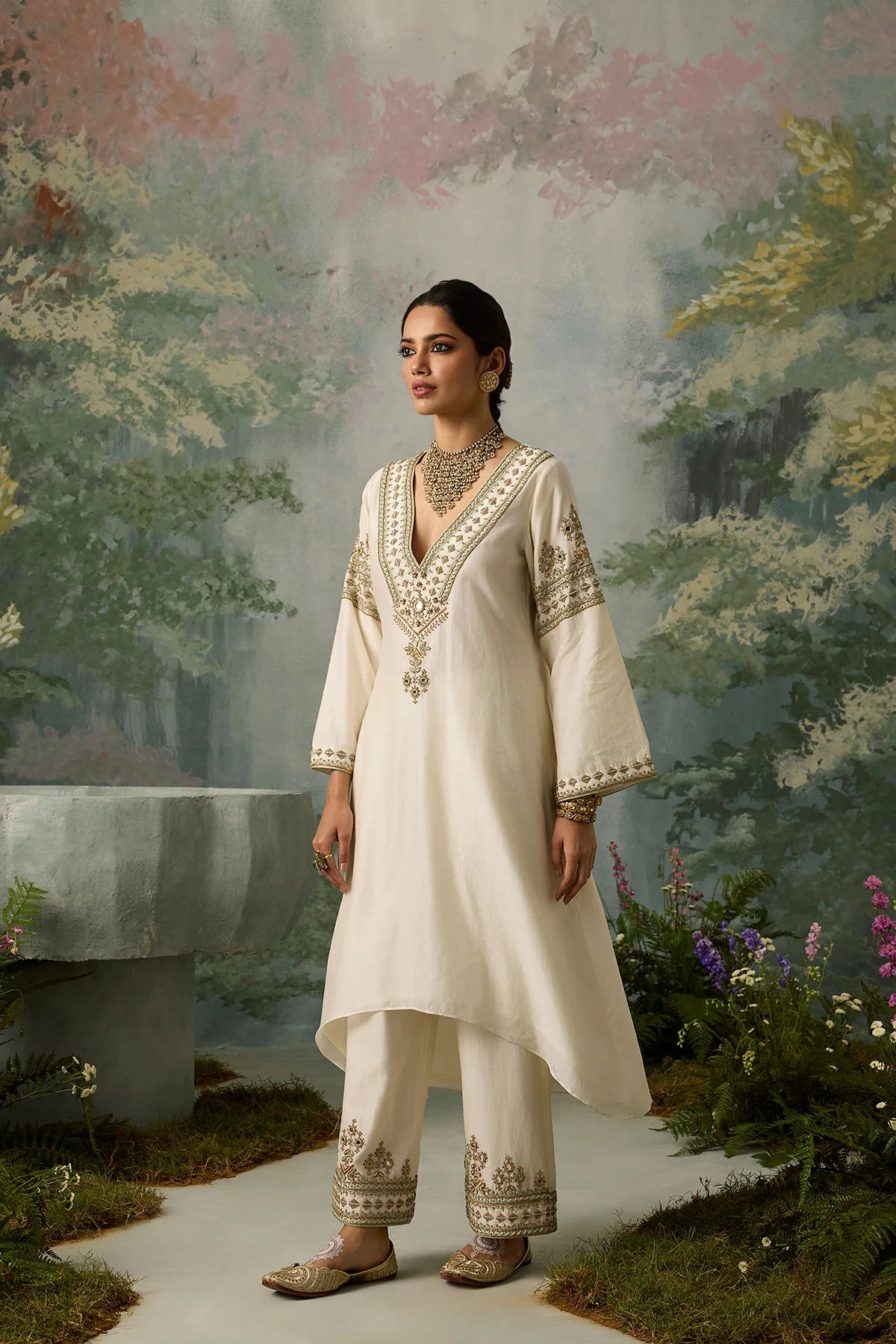 Woman in a traditional outfit standing in a garden with a painted landscape background