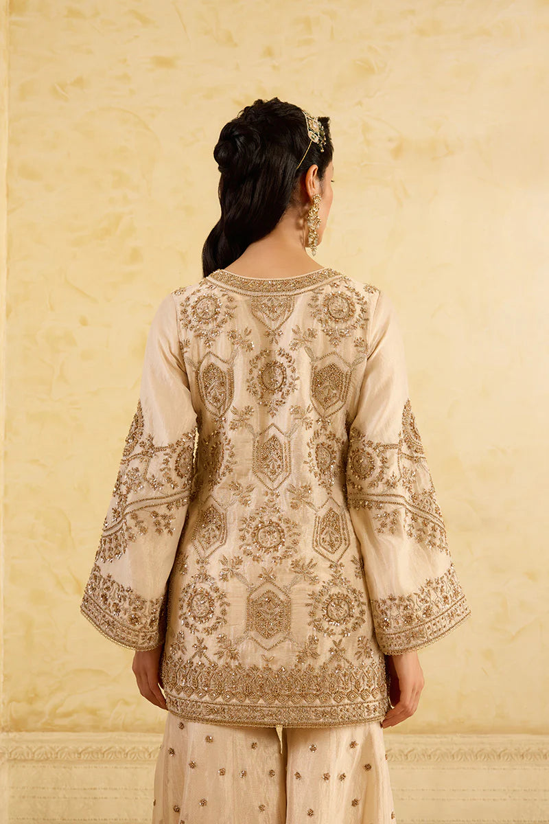 Woman wearing a cream embroidered traditional outfit against a beige background