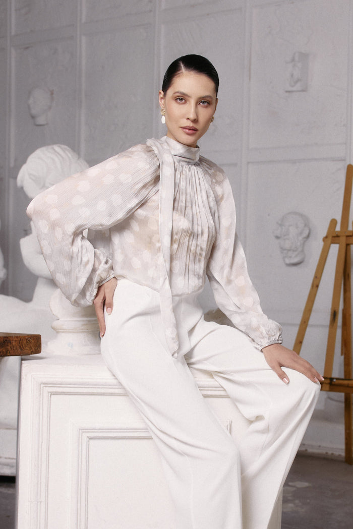 Woman in a white outfit sitting on a white pedestal in a minimalistic setting.