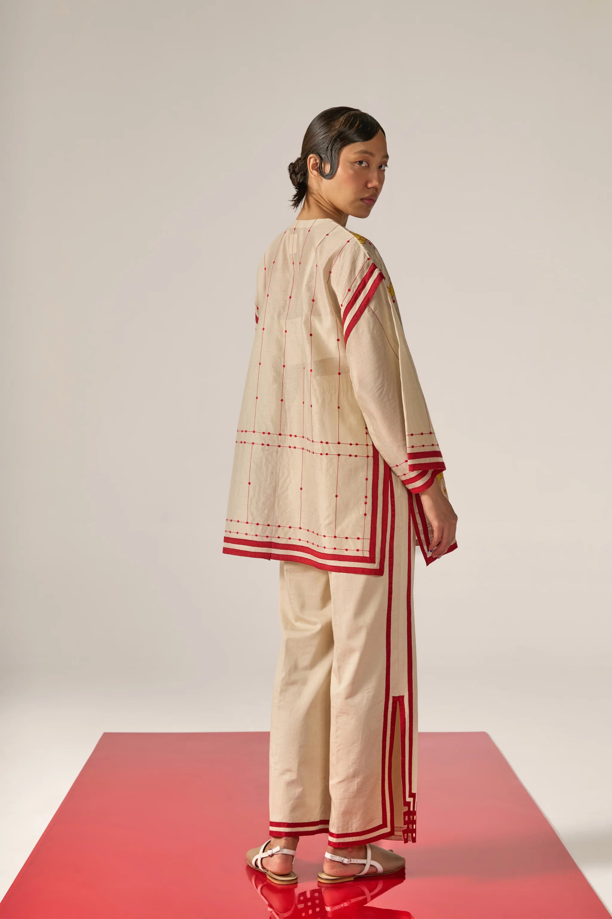 An asian model wearing white Cotton Silk Chanderi shirt featuring a drop-shoulder silhouette with detailed geometric cutwork panels and tonal threadwork along the sleeves and back.