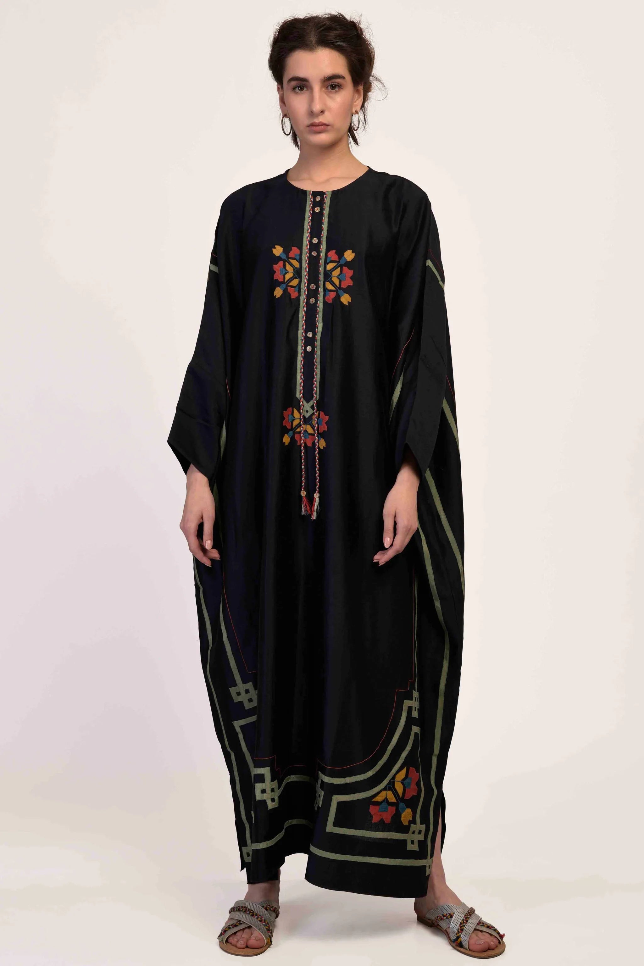 A model in a floor-length black kaftan with intricate geometric hand-cut appliqué in green, red, and yellow tones.