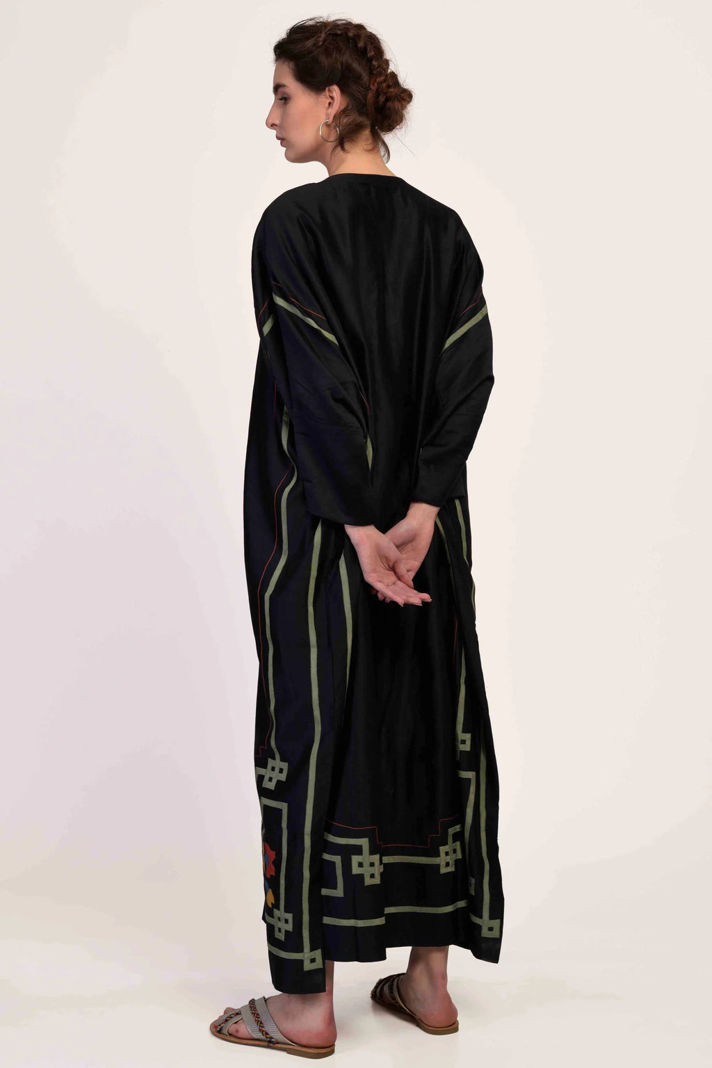 Woman wearing a long black dress with green patterns on a white background