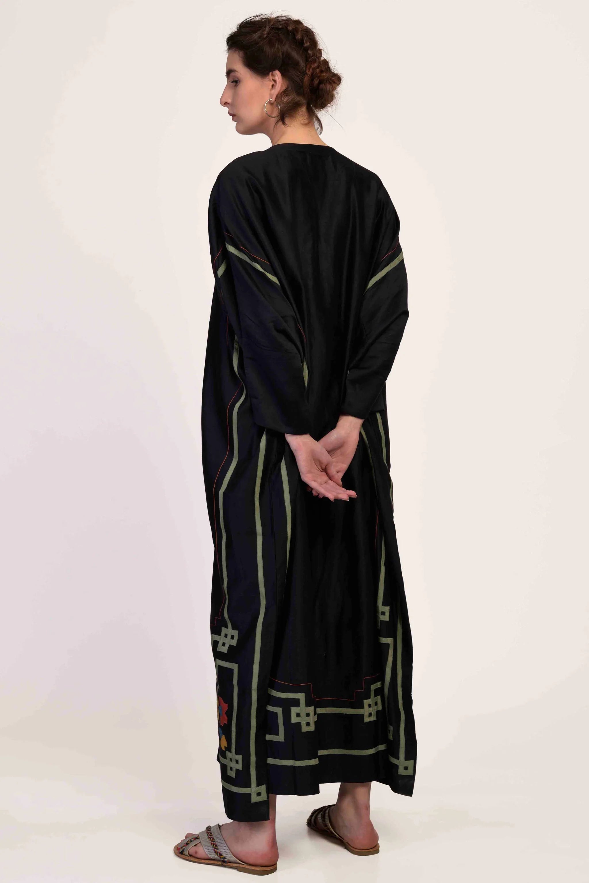Woman wearing a long black dress with green patterns on a white background