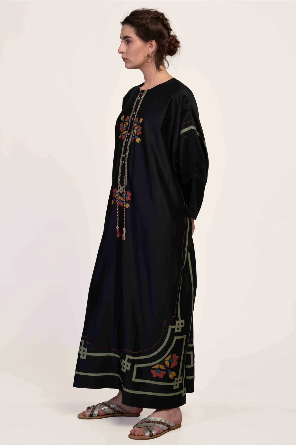 A model in a floor-length black kaftan with intricate geometric hand-cut appliqué in green, red, and yellow tones.