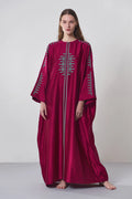 A model wearing a deep maroon long kaftan dress featuring sage green tribal-inspired hand-cut appliqué down the center and sleeves.
