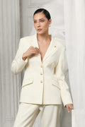 Woman wearing a white suit standing against a white curtain background