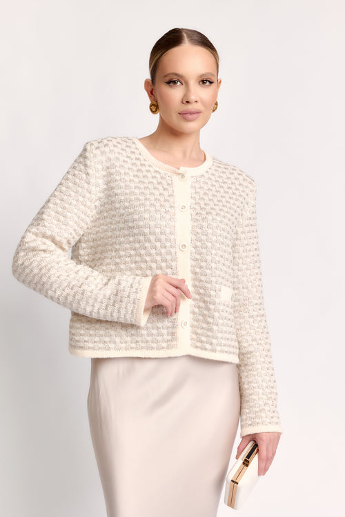 Woman wearing a textured white jacket and skirt set on a plain background