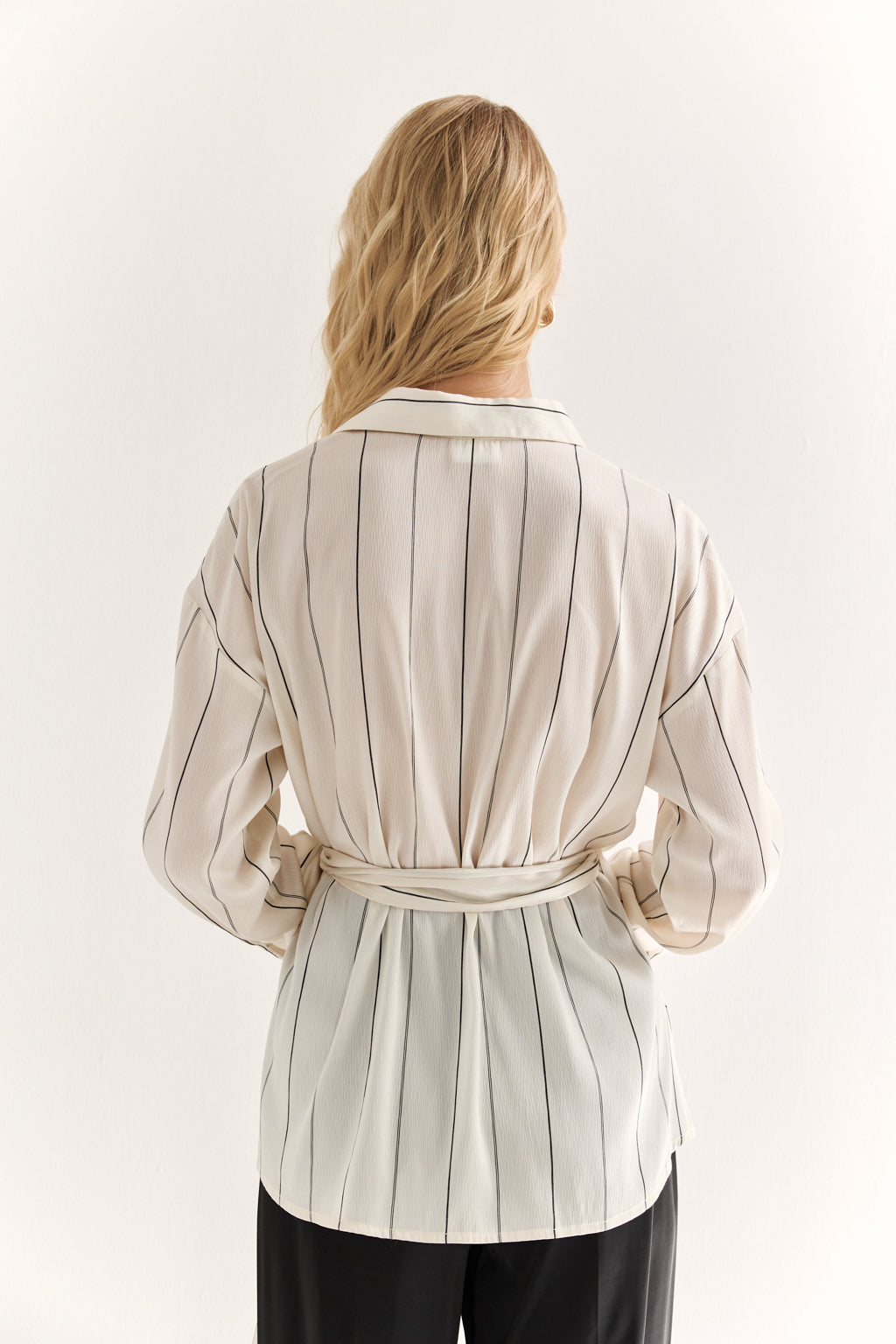 Woman wearing a beige striped blouse with a belt on a white background