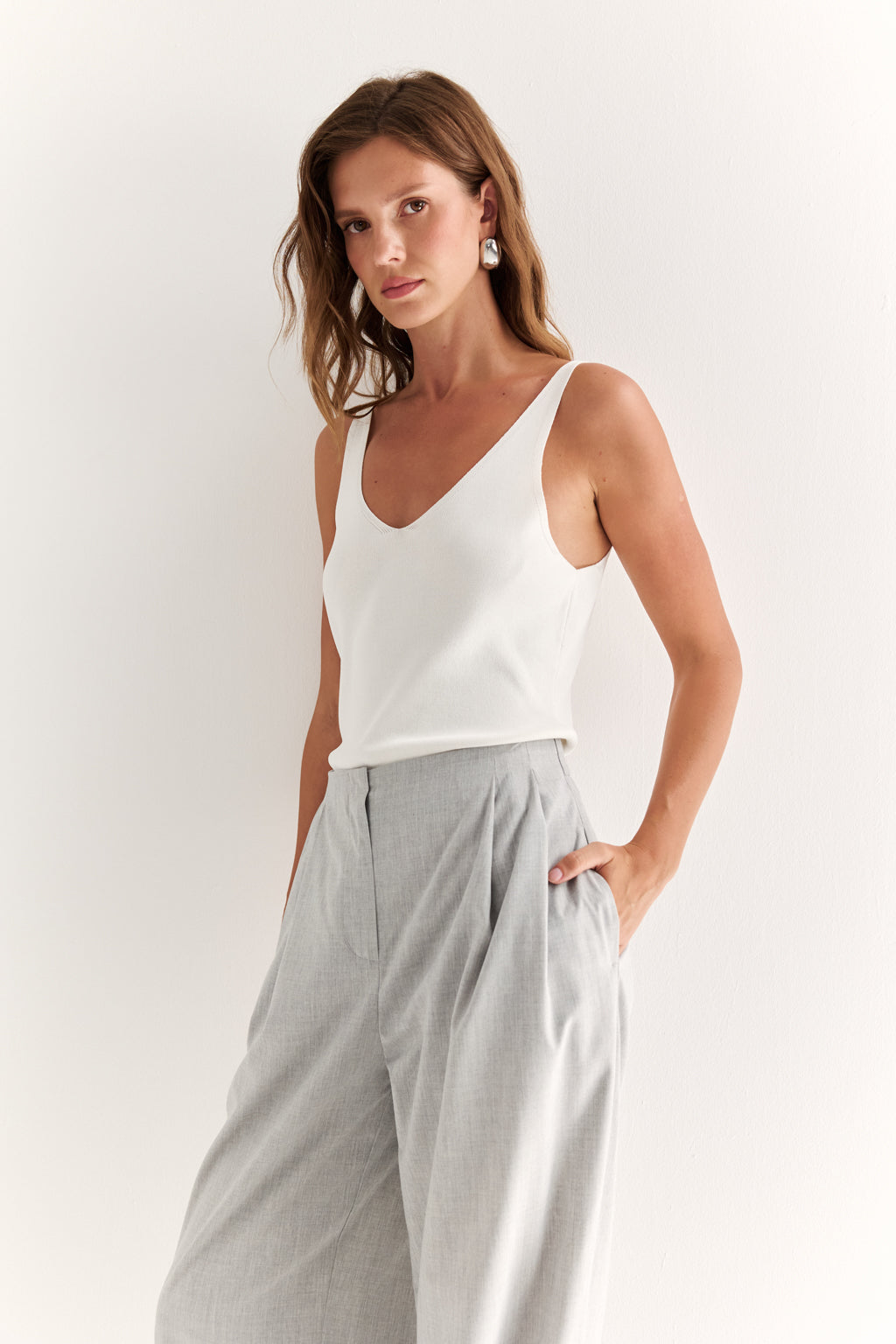 Woman wearing a white sleeveless top and gray pants on a white background