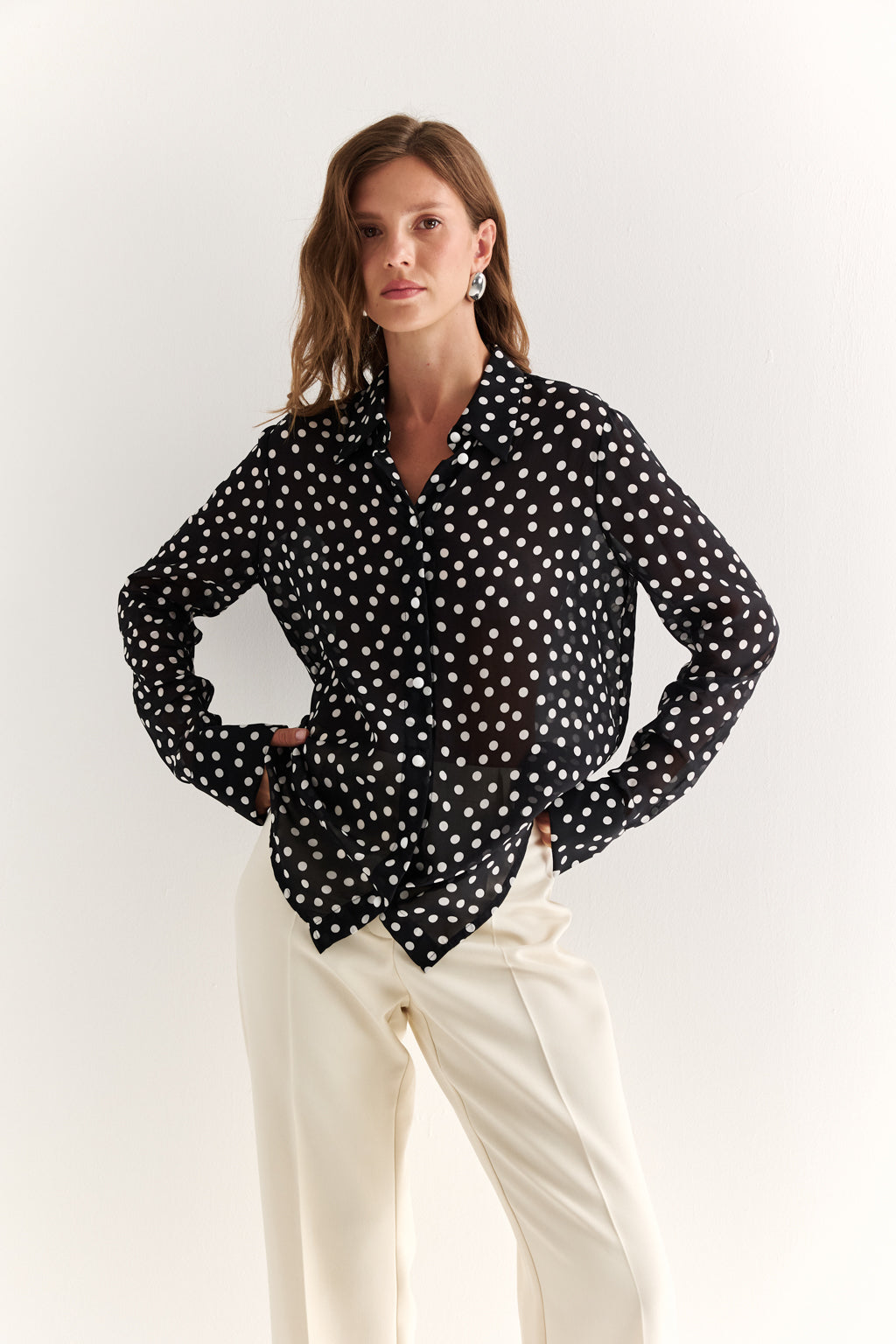 Woman wearing a black polka dot blouse and white pants on a white background