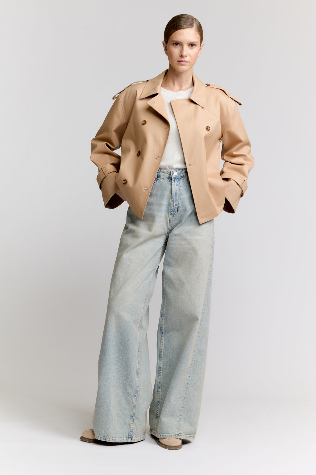 Woman wearing a beige trench coat and light blue jeans on a white background