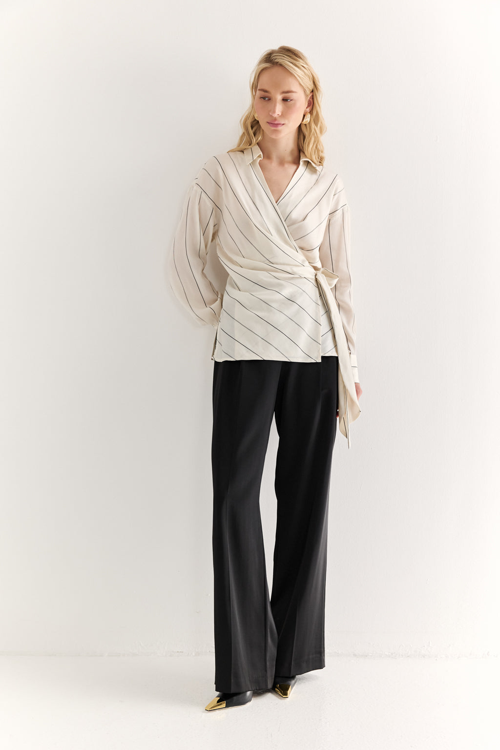 Woman wearing a cream-colored wrap top and black pants on a white background