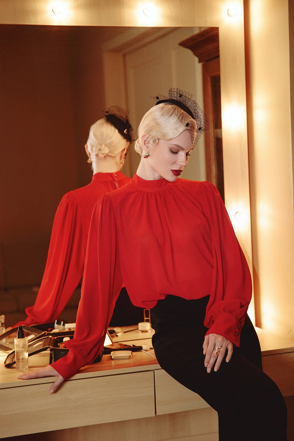 Woman in a red blouse sitting in front of a mirror in a dressing room.