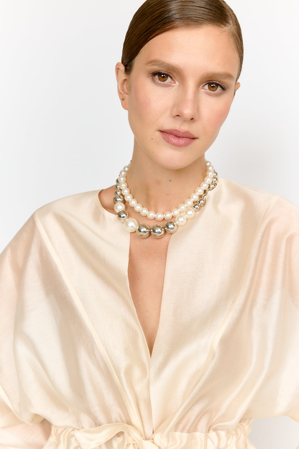 Woman wearing a pearl necklace and beige dress against a plain background