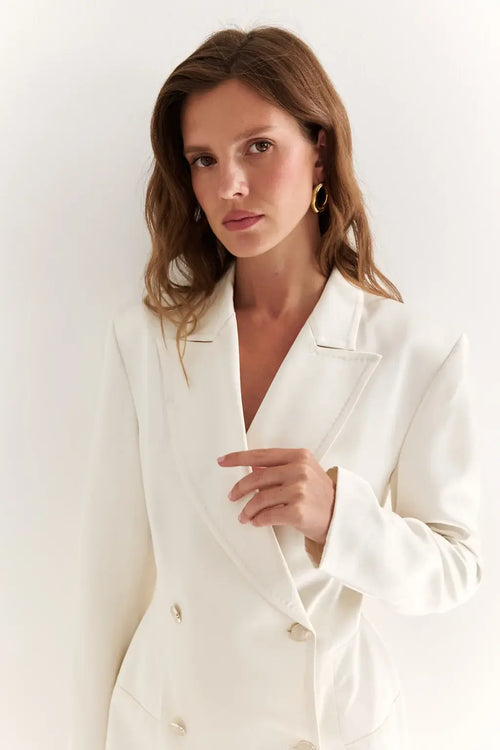 AYRA Store beautiful woman standing wearing  milk-colored double-breasted sculptural luxury jacket dress with architectural shoulders and hourglass silhouette