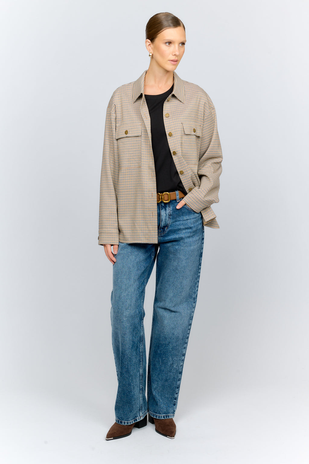 Woman wearing a beige checkered shirt, black top, and blue jeans on a white background