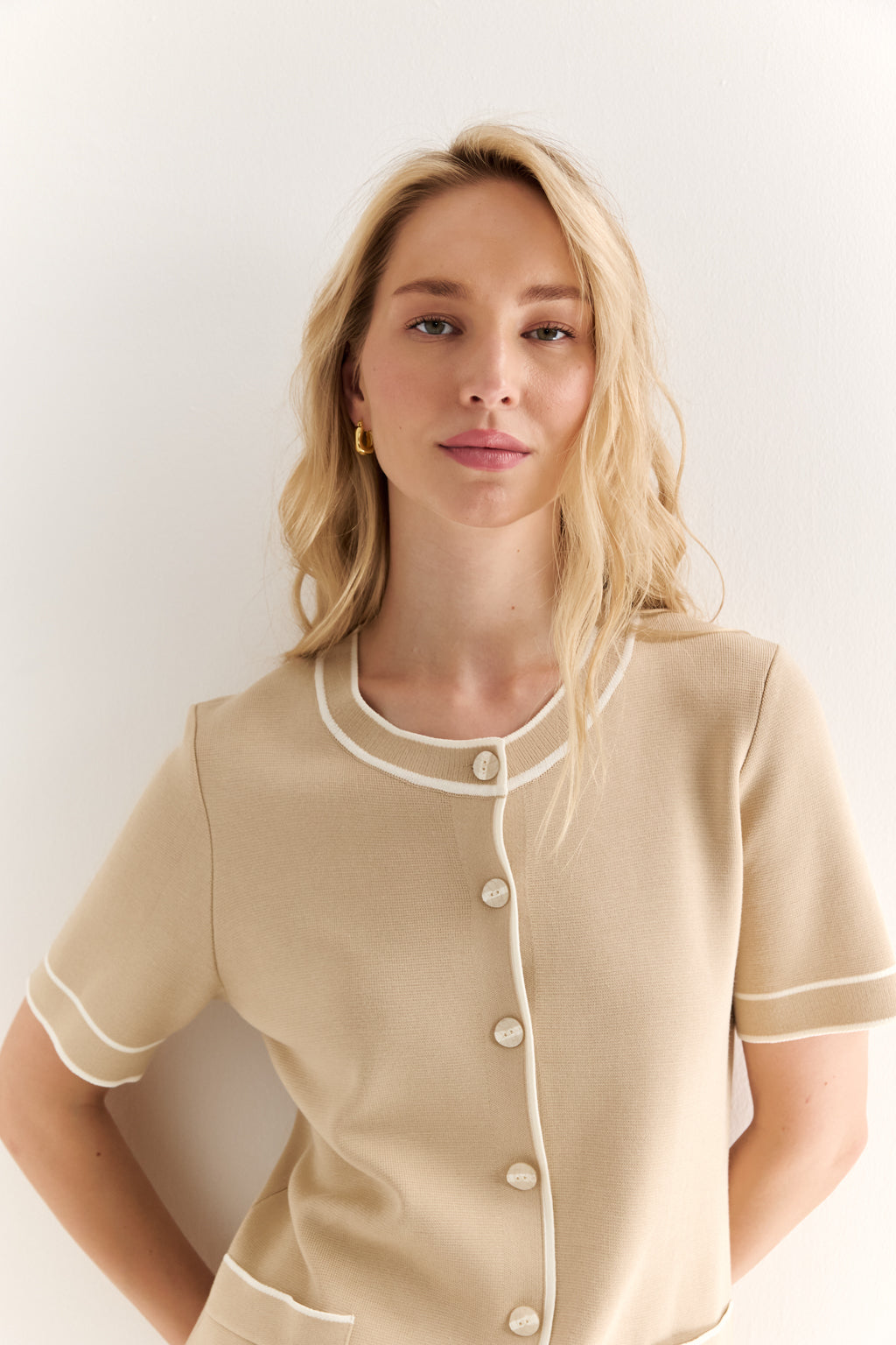 Woman wearing a beige outfit with white buttons against a plain background
