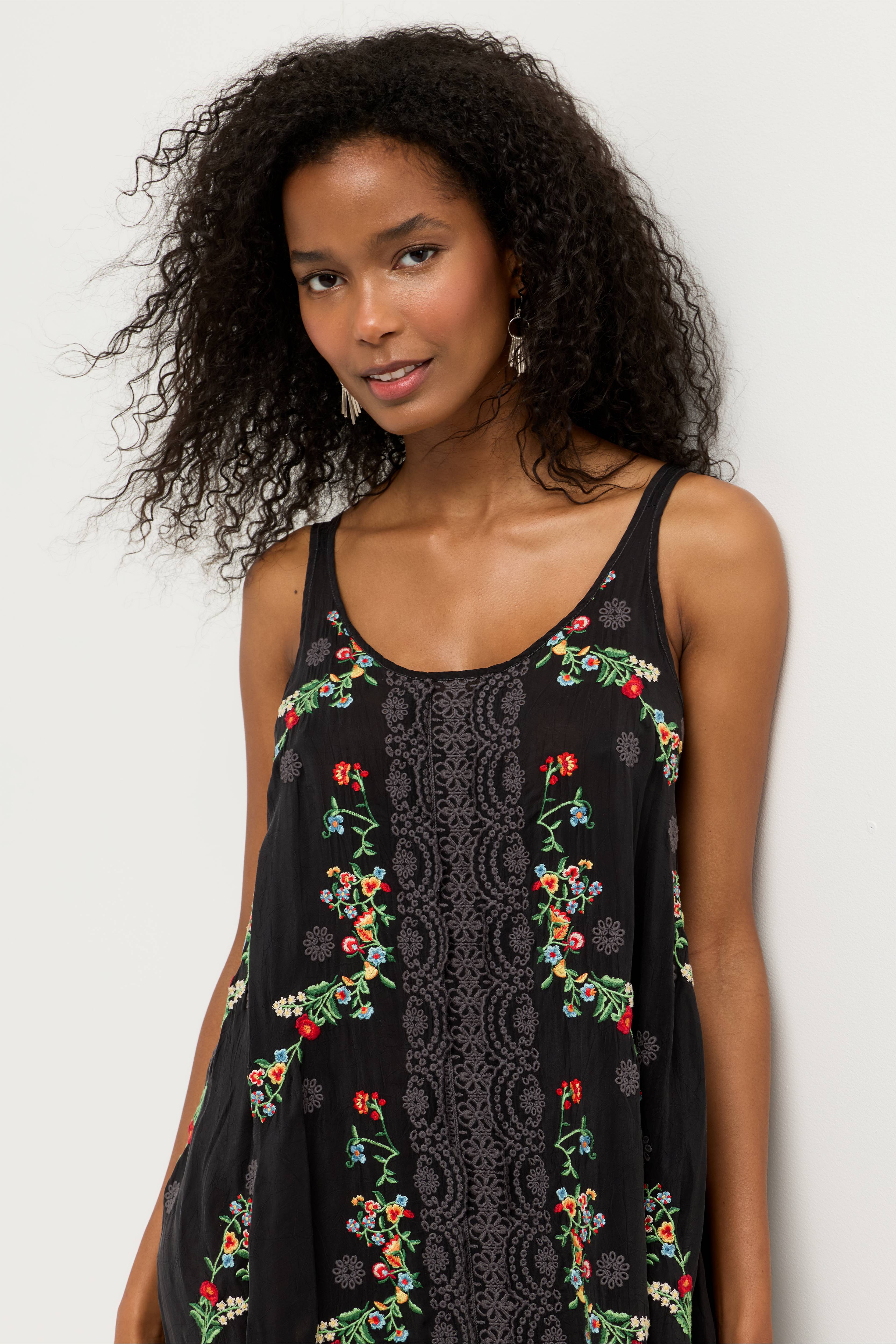 Woman wearing a black sleeveless dress with floral embroidery against a white background