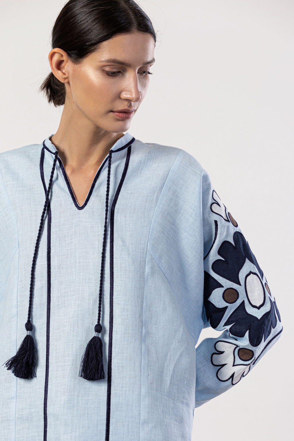 Woman wearing a light blue dress with black tassels and floral embroidery on a white background